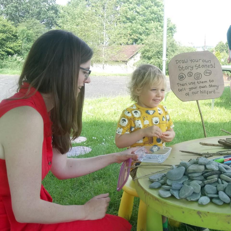 A woman in a red dress with a young child in a yellow top, sitting outside sorting through stones on a table