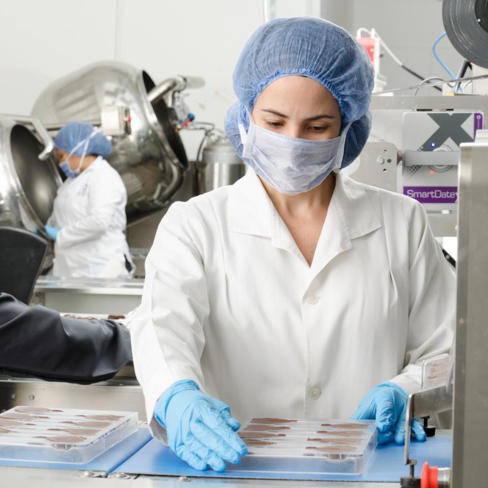 Woman in white coat, hair covering and face mask working in a food factory