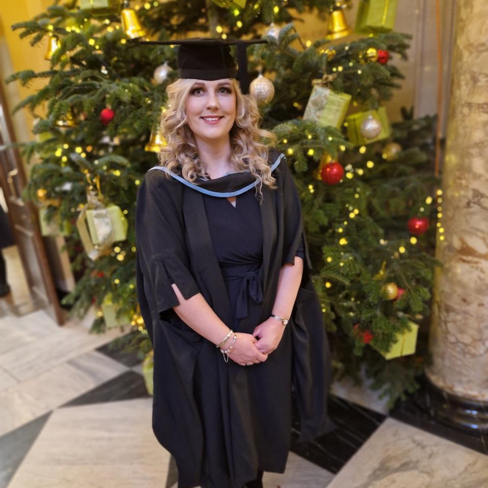 Hayley in graduation cap and gown standing in front of a christmas tree