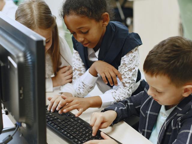 3 young children gathered around a computer