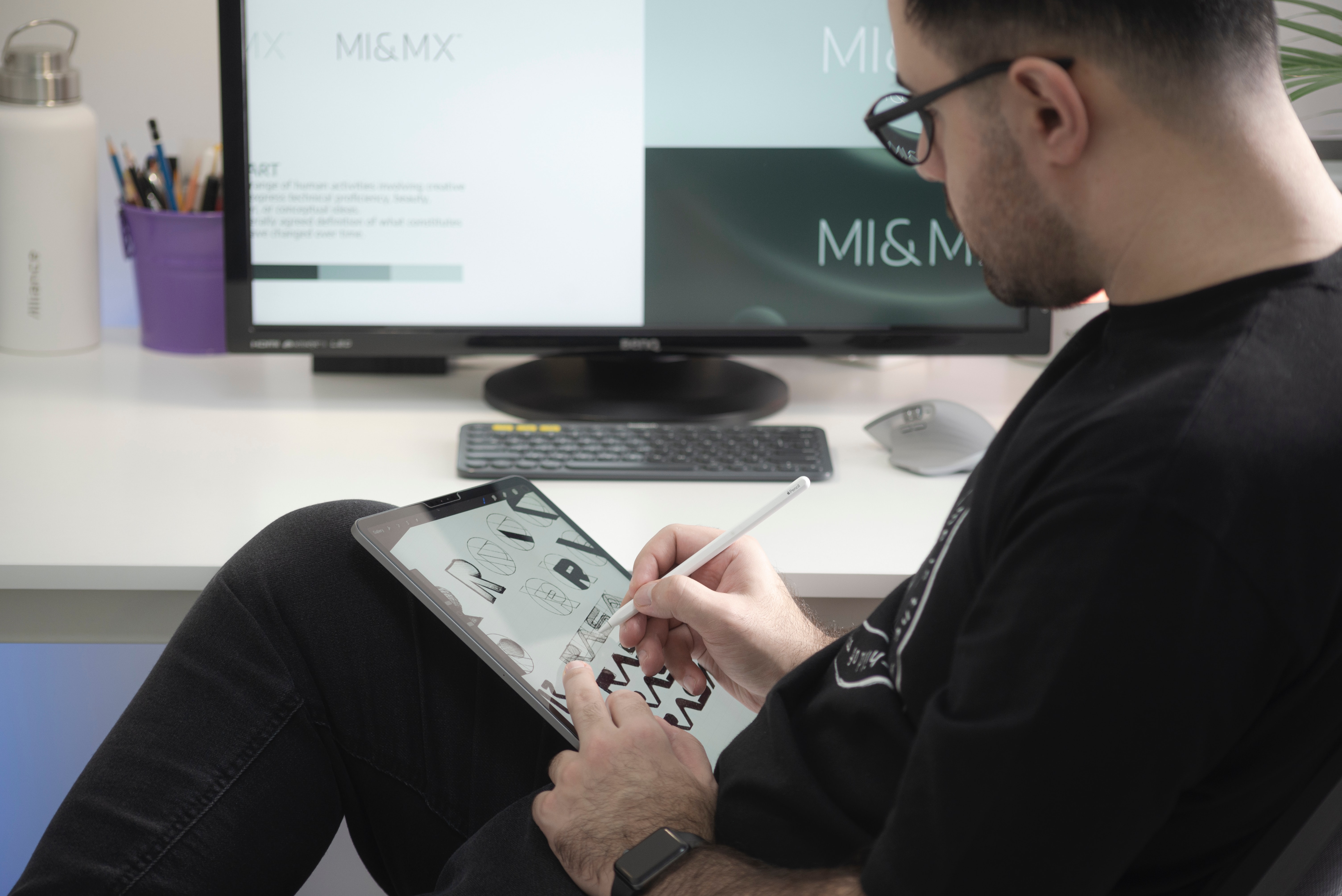 Man dressed in black drawing on a tablet with a computer screen in the background