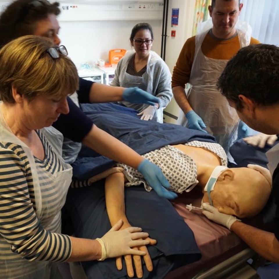 5 people in plastic aprons working on a dummy in a simulation suite