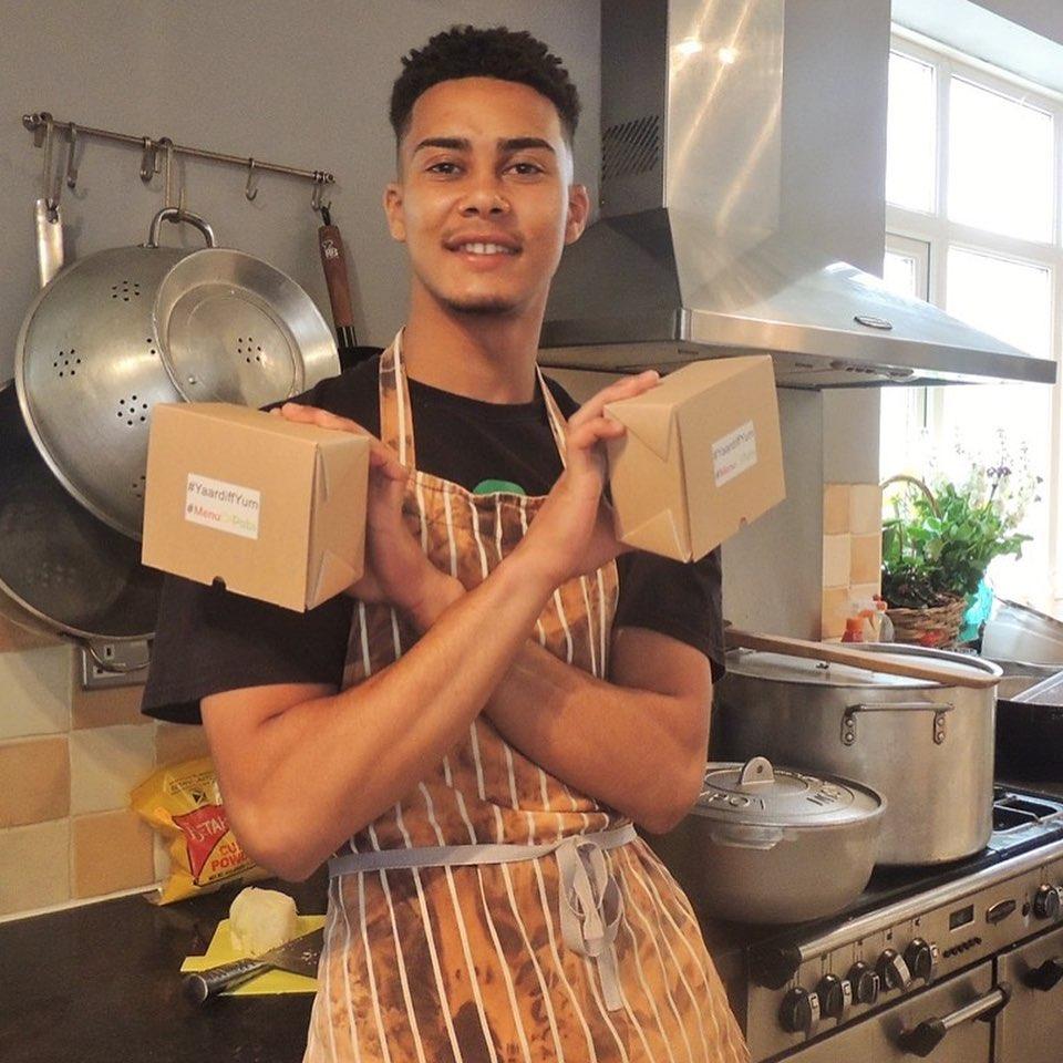 Man in kitchen wearing an apron and holding two food boxes