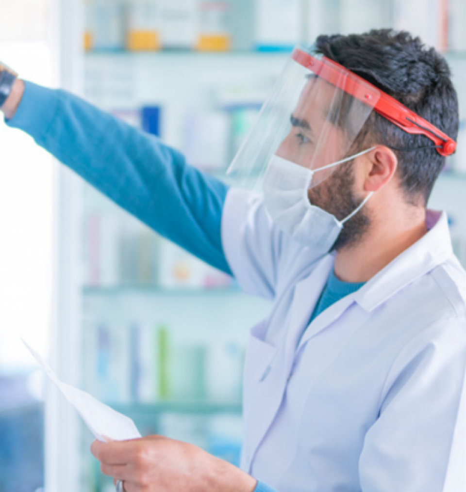 Man in lab coat, face mask and visor working in a dispensary