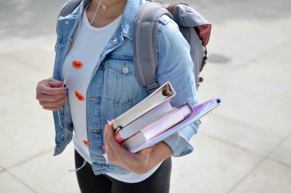 A student wearing a backpack and holding a stack of books