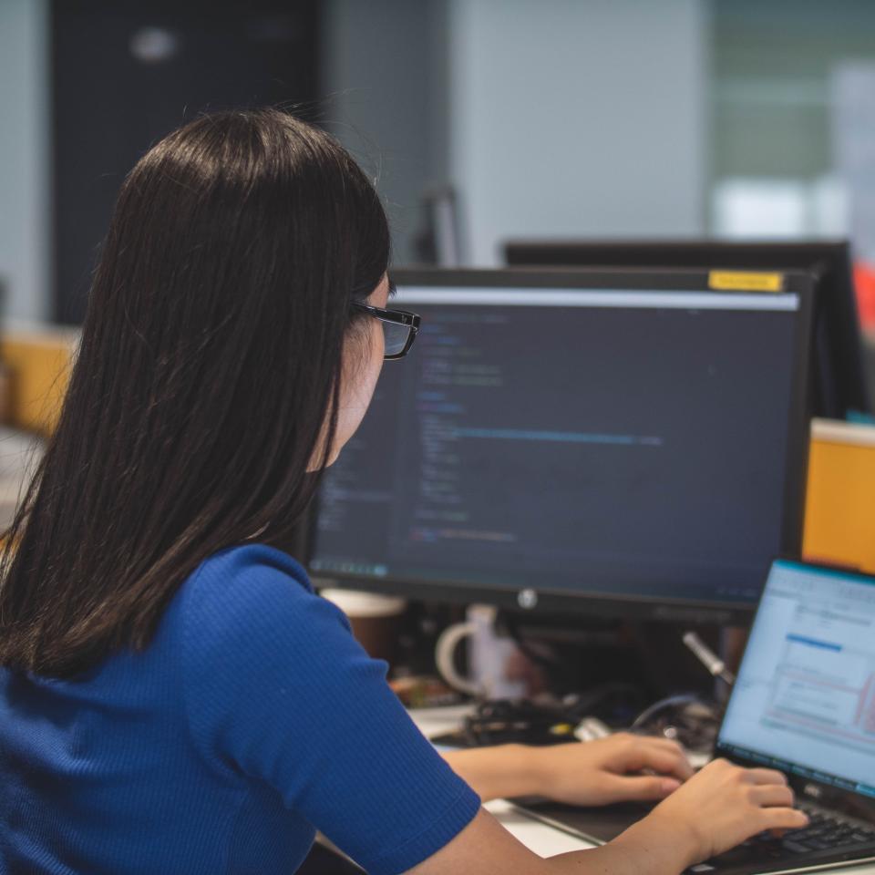 Young woman in blue top sitting at a desk working on a computer