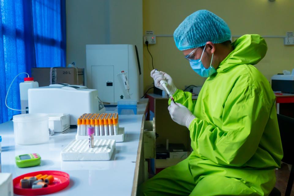 Scientist wearing green overalls and blue cap working in a lab