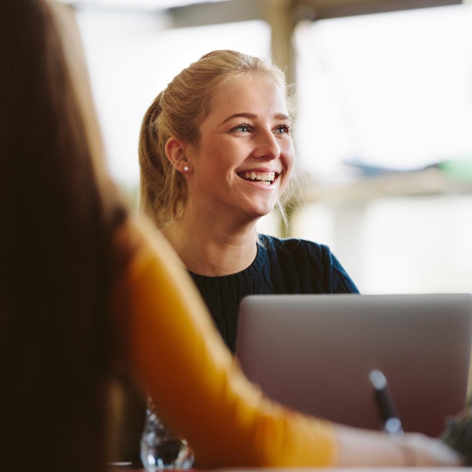 Woman with blonde hair smiling, sitting in front of a laptop