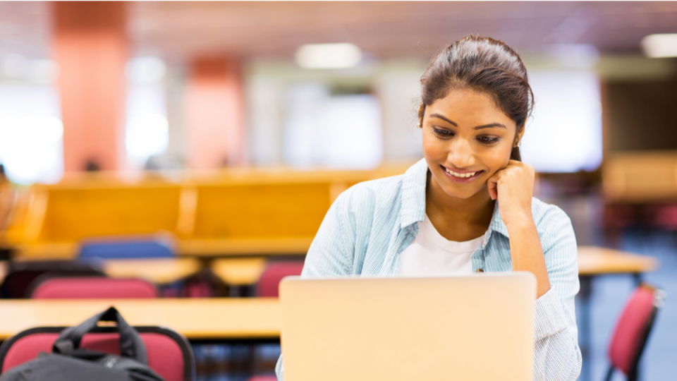 Young woman smiling and working on a laptop in a library