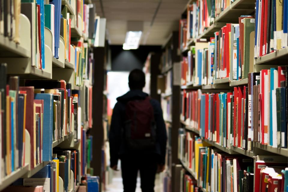 A person in silhouette walking amongst shelves of library books