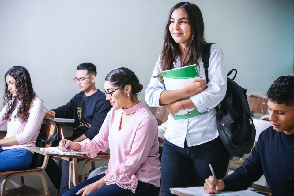 Young woman holding a book walking through a class of students