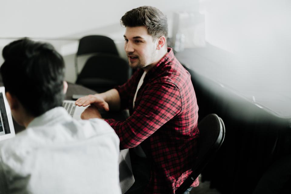 2 men sitting at a table with laptops