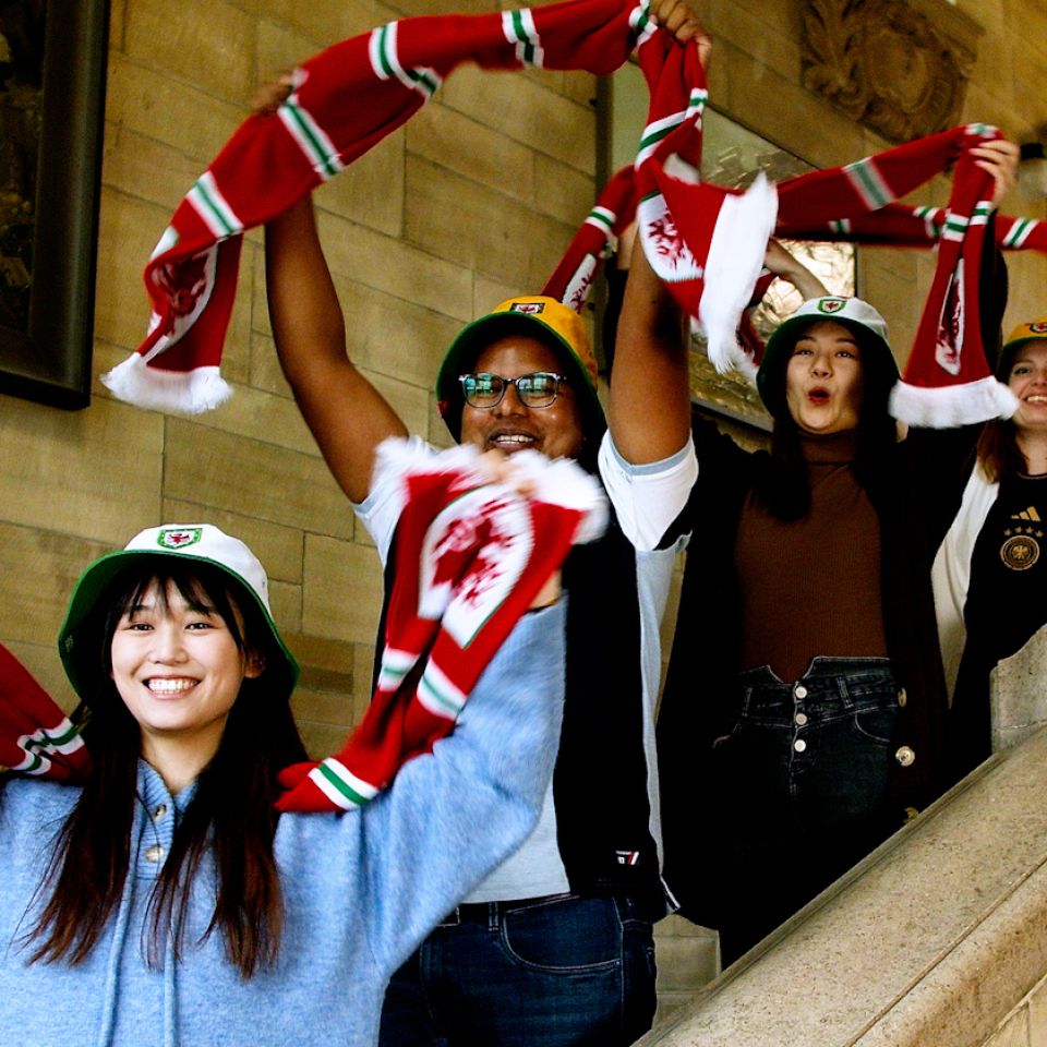 International students cheering and waving Wales scarves. 