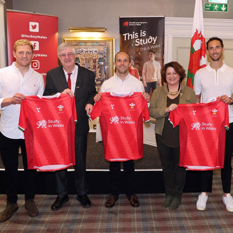 Wales men's hockey players with First Minister of Wales, Mark Drakeford, holding hockey shirts featuring the Study in Wales logo.