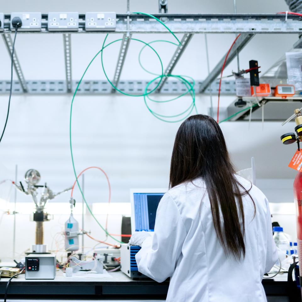 Female engineer in white coat working at a lab bench, with back to camera