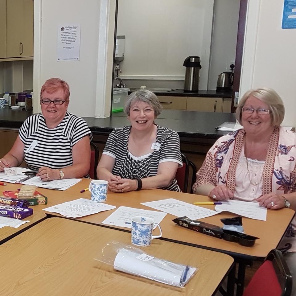 A group of smiling women sitting and standing around a meeting table