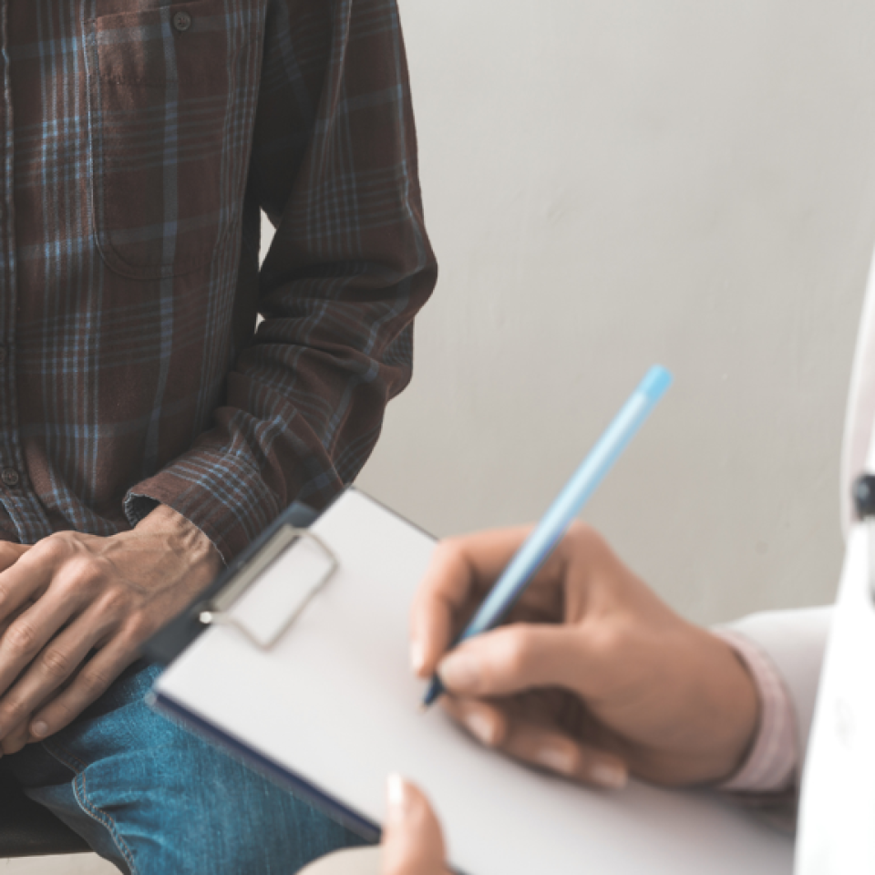 A man sitting on a bed with a doctor writing on a clipboard