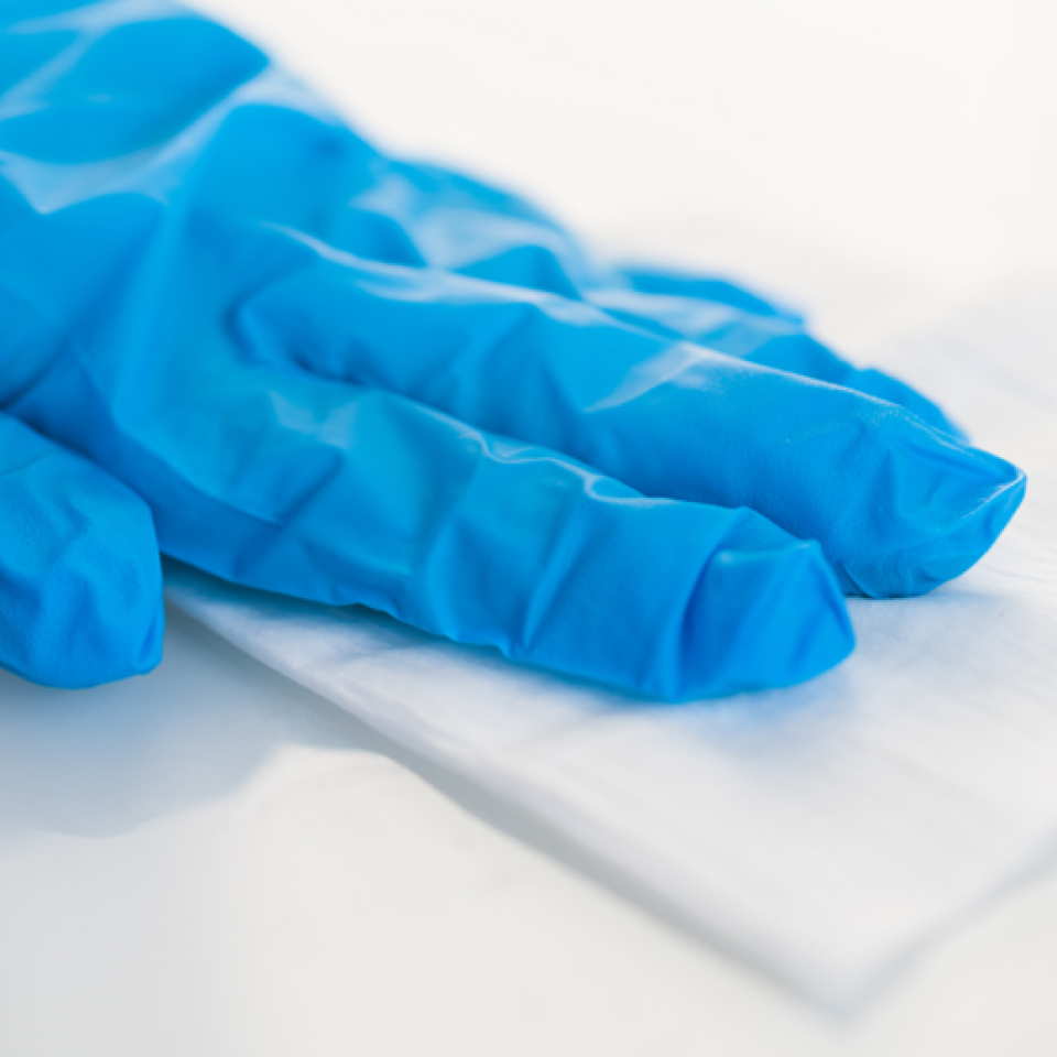 A hand in blue glove using a wipe on a white surface