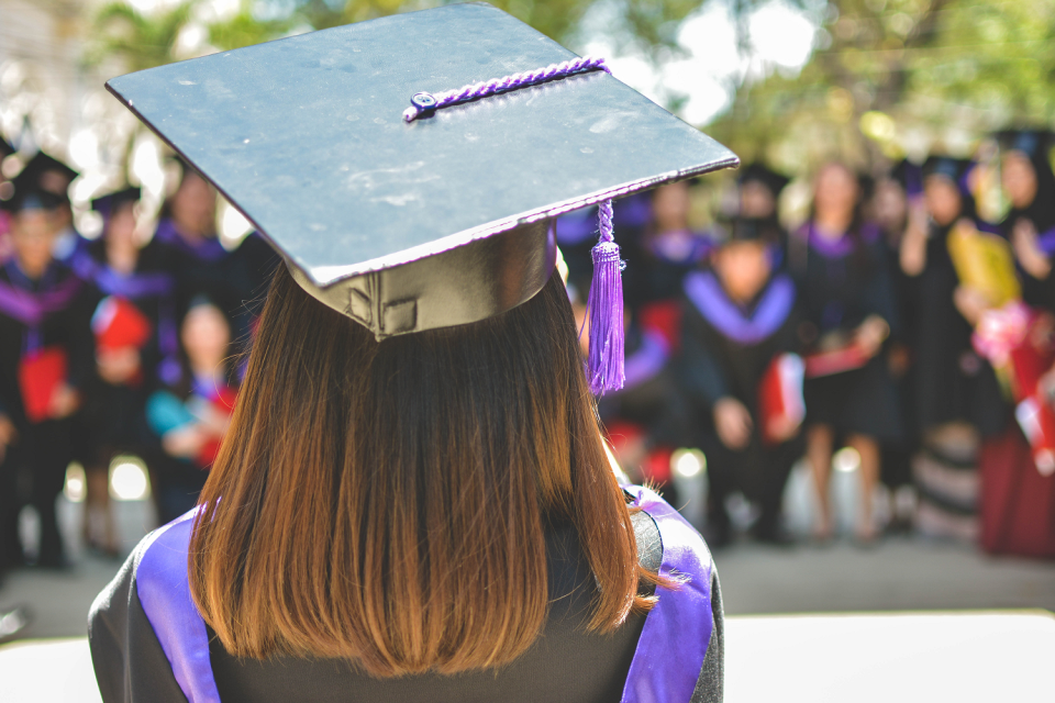 A graduate in cap and gown with back to camera, facing a crowd of other graduates