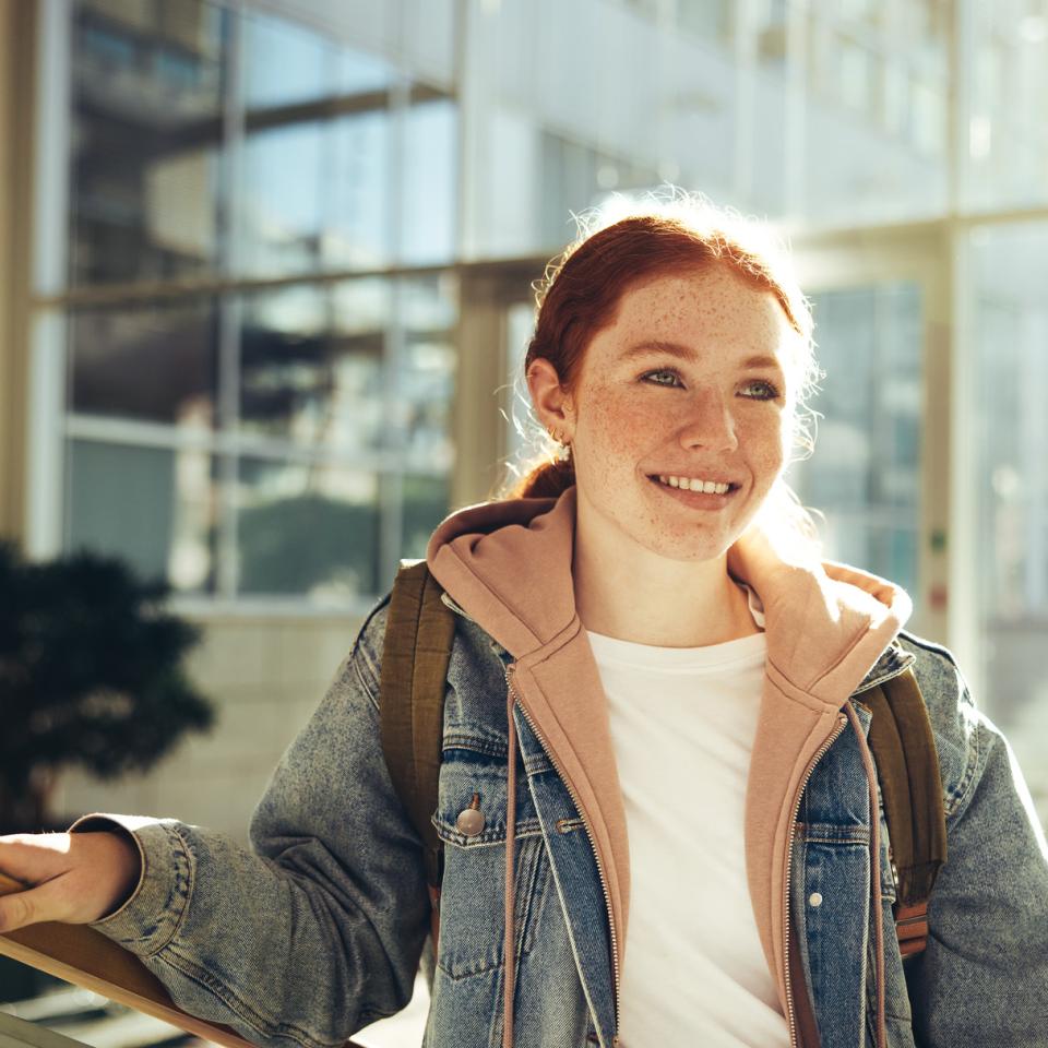 A smiling young woman standing in front of large windows