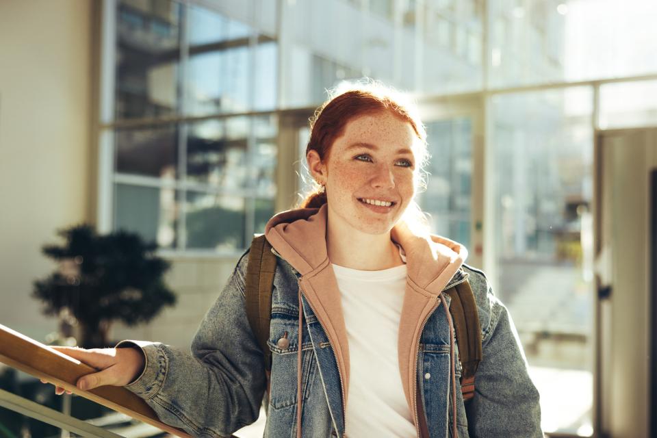 Photo of young woman in denim jacket smiling and standing in a public building