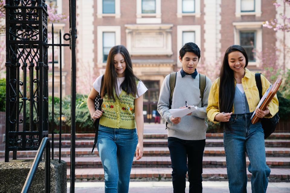 three students (one man, two women) walking together outside a building