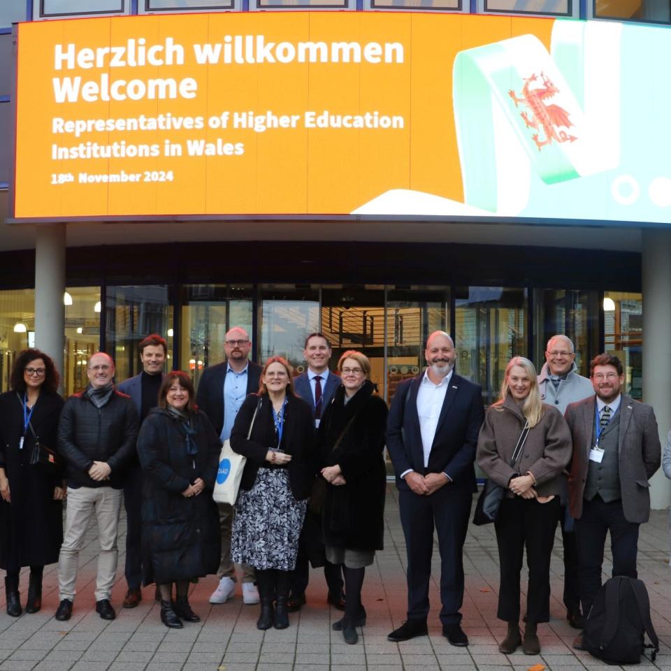 Delegation underneath a sign that welcomes the representatives of higher education institutions in Wales