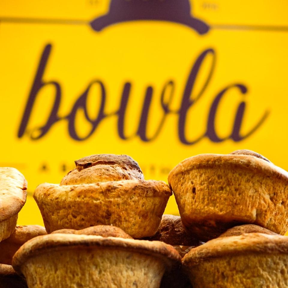 A stack of bread rolls in front of a yellow sign with the 'bowla' logo