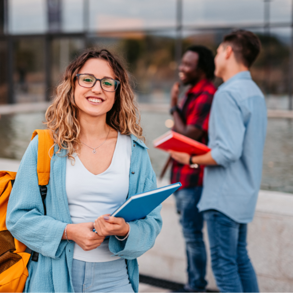 A smiling woman holding a book. Three other people are in the background smiling and talking