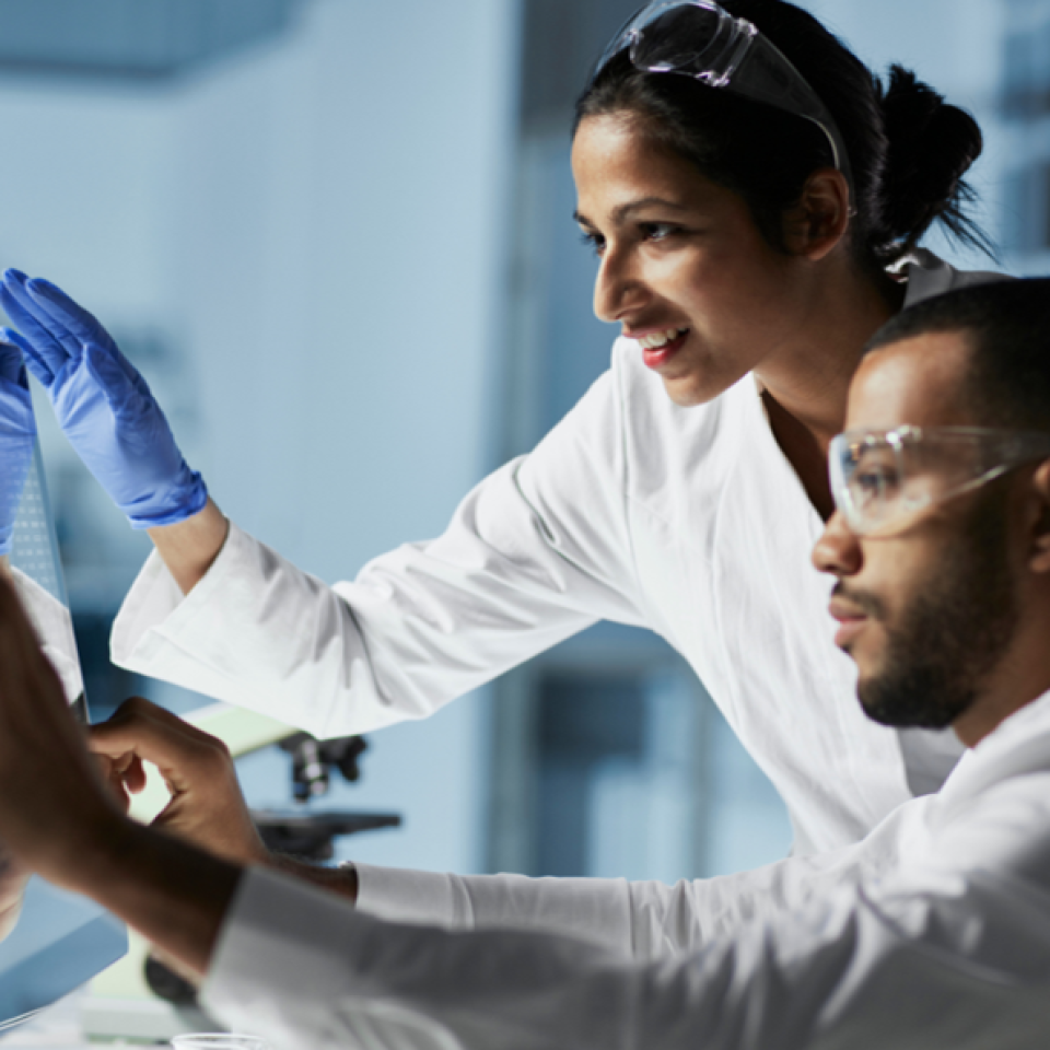 A man and woman in lab coats working at a screen