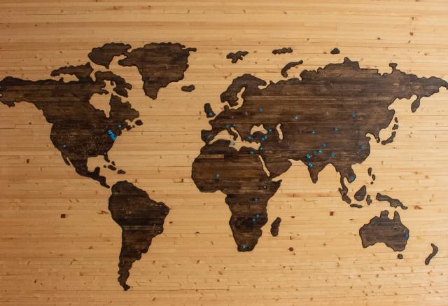 A map of the world on a wooden background with blue pins stuck in lots of countries