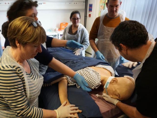 5 people in plastic aprons working on a dummy in a simulation suite
