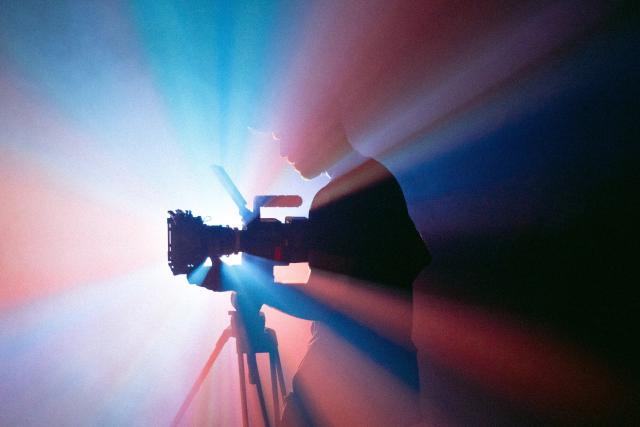 Silhouette of someone operating a TV camera with background of coloured lights
