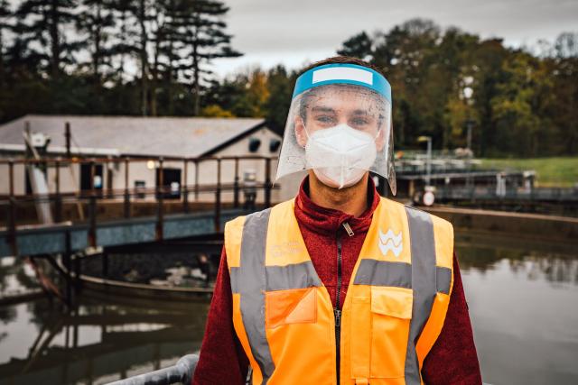 Man in hi-vis vest and visor standing by a reservoir