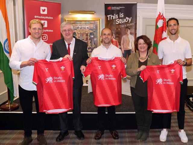 Wales men's hockey players with First Minister of Wales, Mark Drakeford, holding hockey shirts featuring the Study in Wales logo.