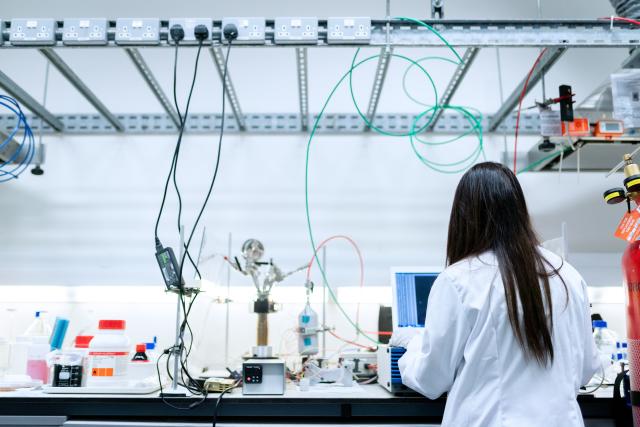 Female engineer in white coat working at a lab bench, with back to camera