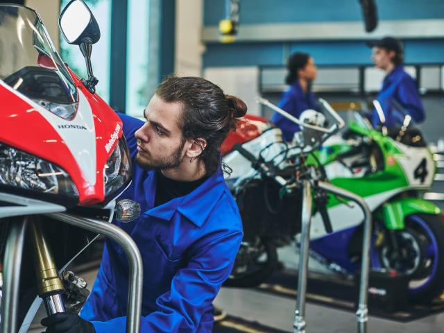 A mechanic in blue overalls is working on a motorbike