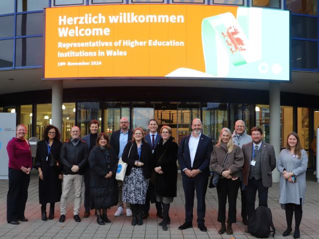 Delegation underneath a sign that welcomes the representatives of higher education institutions in Wales