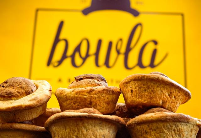 A stack of bread rolls in front of a yellow sign with the 'bowla' logo