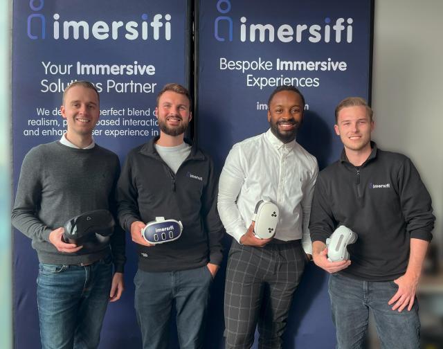 Four men holding VR headsets standing in front of imersifi banners