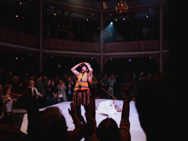 A man in a hi-vis vest, performing on a stage in front of a full theatre