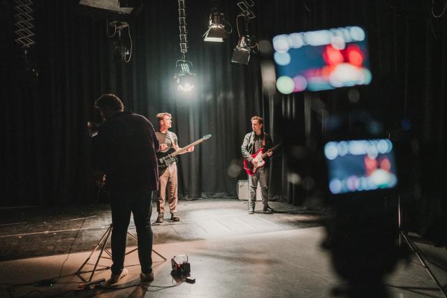 A TV studio stage with a cameraman and 2 people playing guitar