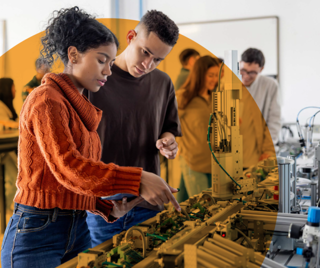 A male and female in a large room looking at equipment. Other students are in the background
