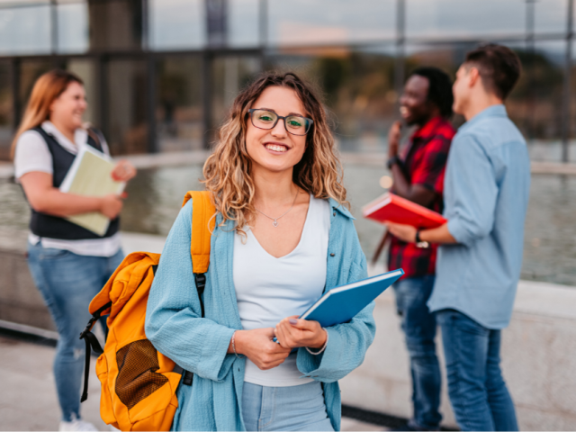 A smiling woman holding a book. Three other people are in the background smiling and talking